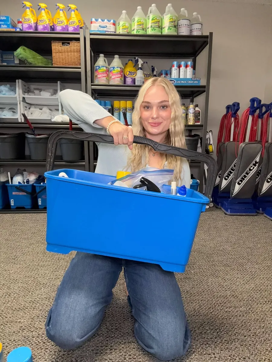 Maigan kneeling in her company's supply room with a cleaning caddy